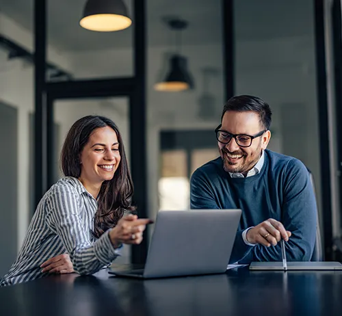 Two professionals smiling and collaborating on a laptop in a modern office